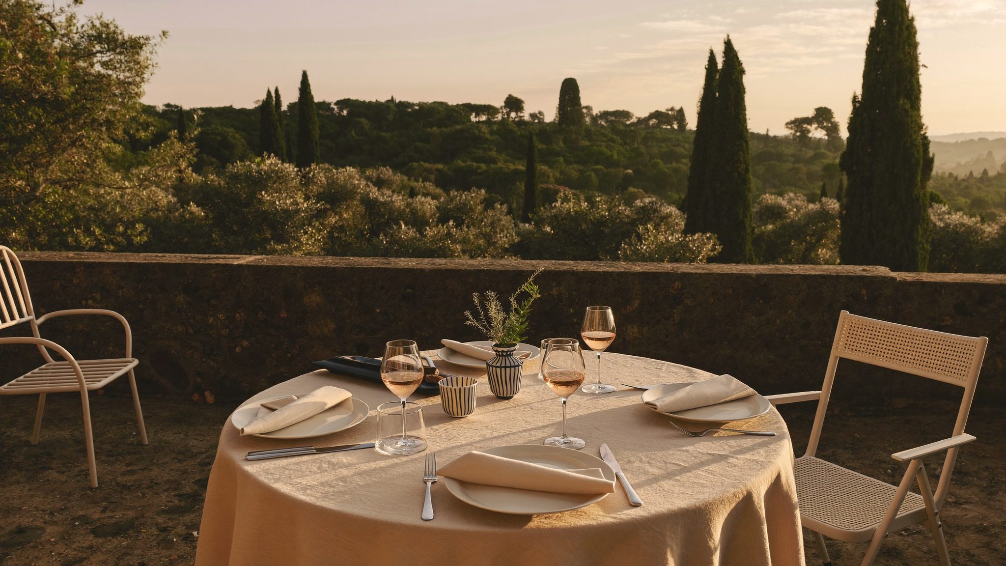Table dressée pour deux sur une terrasse en pierre au-dessus de la mer, en fin de journée